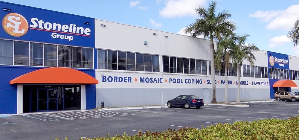 A large commercial building with “Stoneline Group” signage, blue and white exterior, orange awnings, palm trees, and a parking lot with cars in front, promoting quality stone products like border, mosaic, and travertine.